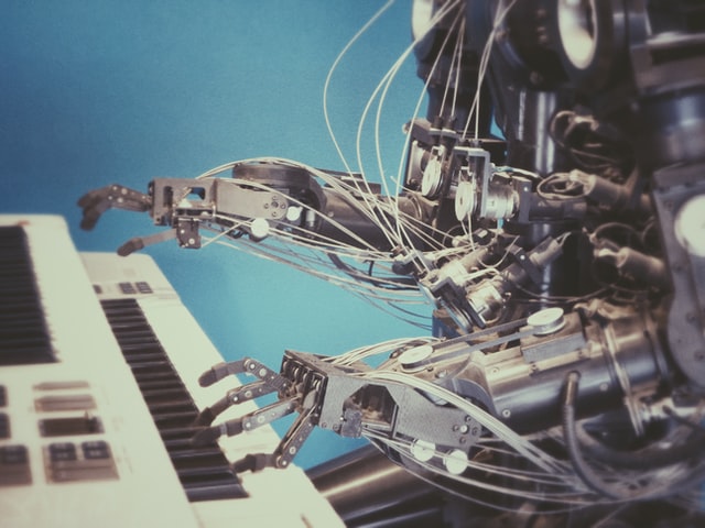 A robot with extended metal fingers resting on the black keys of a yellow keyboard